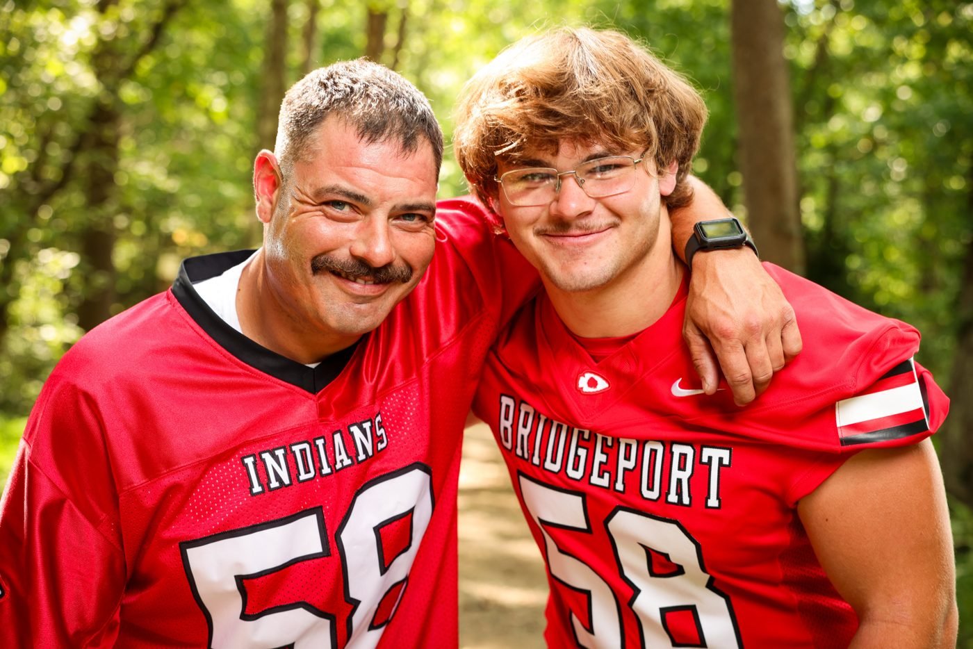 Father and son in matching red Bridgeport football jerseys on a wooded trail