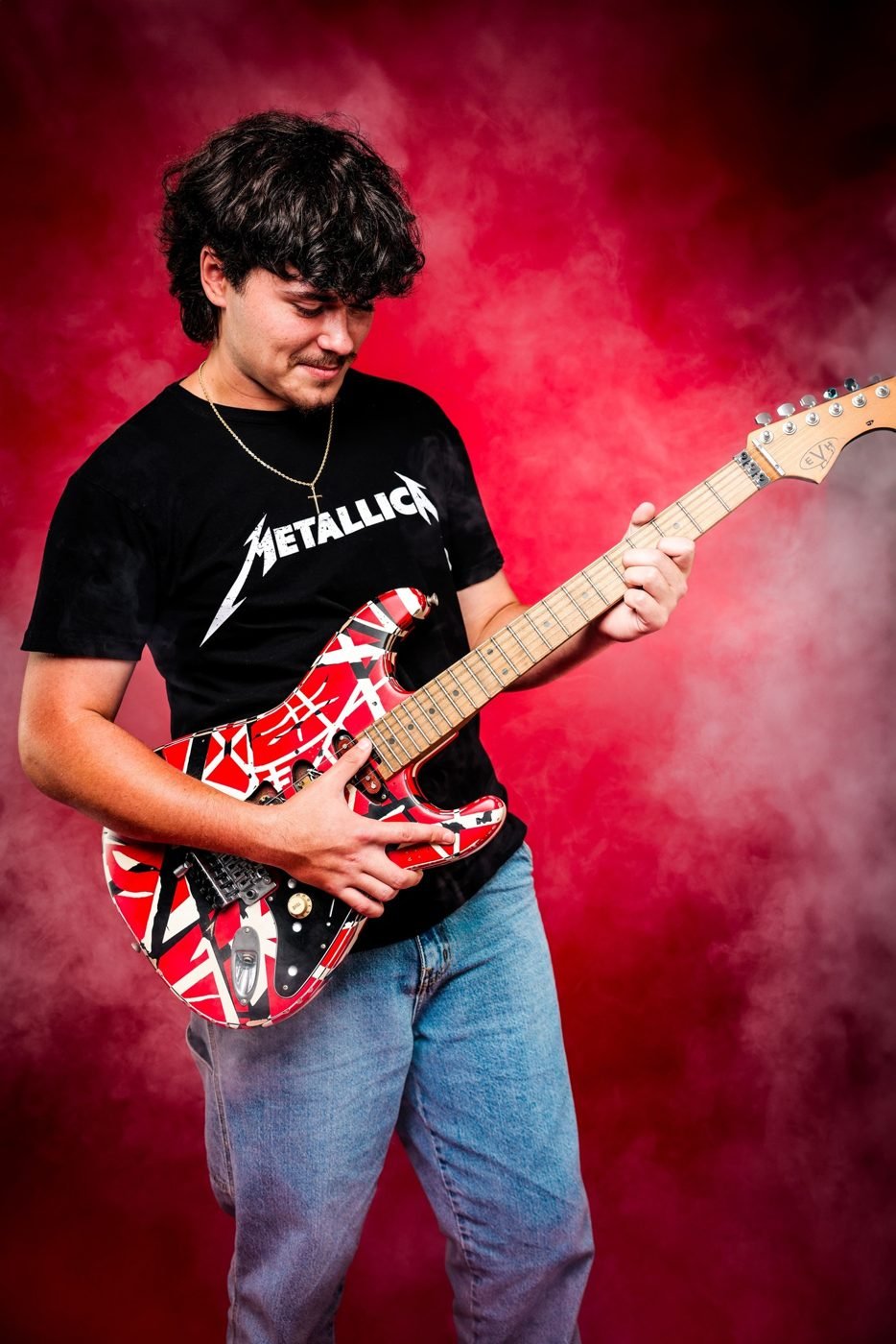Senior portrait of a young man playing a striped electric guitar against red smoke