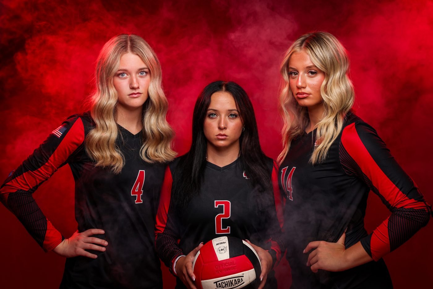 Three volleyball seniors in black and red uniforms under red studio light